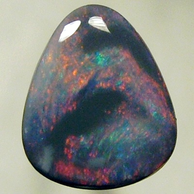 SOLID BLACK OPAL Black opal surrounded by sparkles of red on a green background