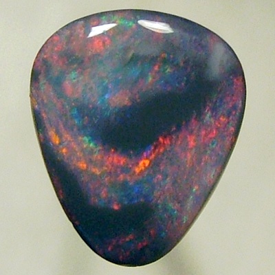 SOLID BLACK OPAL Black opal surrounded by sparkles of red on a green background